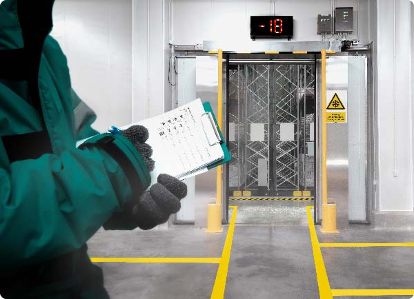 A worker who is wearing gloves and a coat is marking items off a list in a freezing warehouse. The warehouse is neatly sectioned into different areas using ToughStripe Cold floor tape.