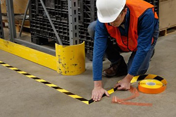 A worker marking an area of a manufacturing facility with yellow and black striped tape.