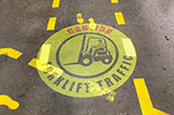 A caution forklift traffic sign projected onto a walkway within a manufacturing environment.