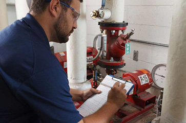 An OSHA inspector checks pipes for proper valve tagging and pipe labeling.