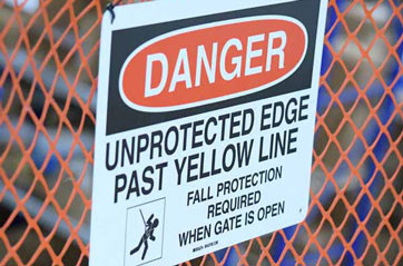 A warning sign on a fence indicating a danger zone beyond the yellow line, highlighting an unprotected edge.