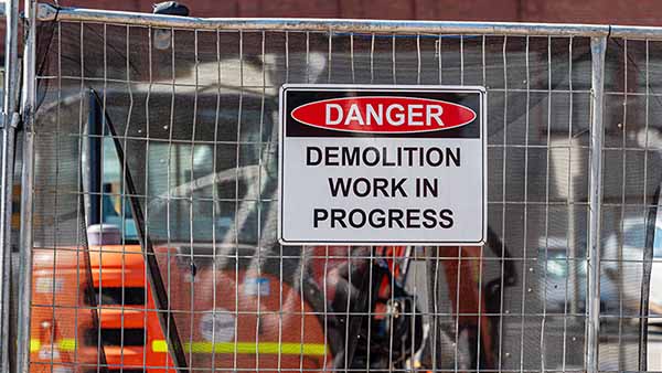 A construction label sign reads, “Danger, demolition work in progress” on a construction site.
