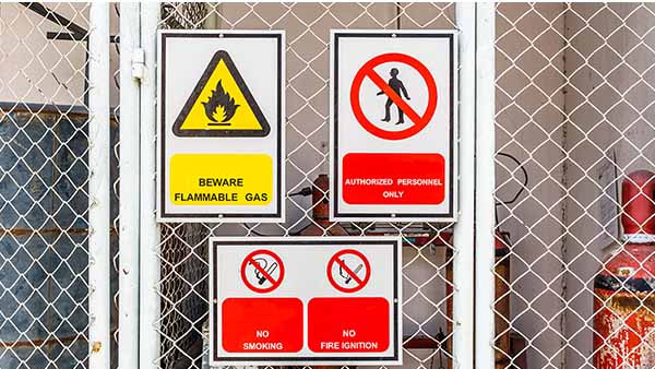 Three safety signs indicating flammable gas, authorized personnel, and no smoking hang on a fence that protects construction site workers from stored material hazards.