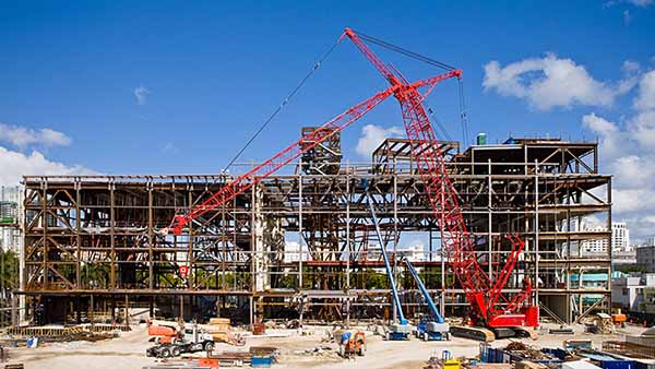A red crane on a construction site building a steel frame building.
