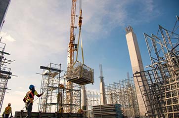 A group of construction workers in safety uniforms install reinforced steel columns on a construction site with hazards.