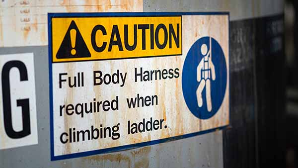 Safety caution sign for a construction jobsite that requires full body harness before climbing ladder to work at height to prevent fall hazards.