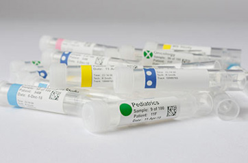 Lab specimen tubes lay in a pile, each with unique label color codes that have been applied with a laboratory label printer.