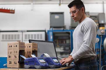 A man in a warehouse setting is creating heat shrink labels on Brady M611 label printer.