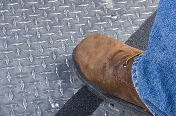 A person stepping over a tape line on a grated metal floor.