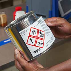 A person applies a GHS diamond label to a metal can.