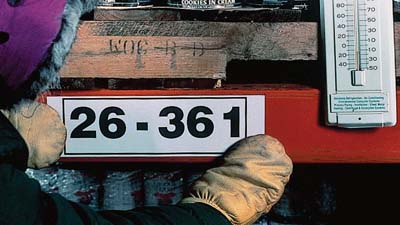 A person wearing mittens applies a label inside a freezer.