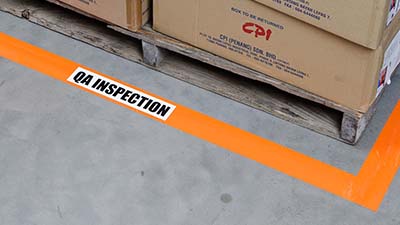 Pallets of materials are sectioned off with floor tape and a label for QA inspection.