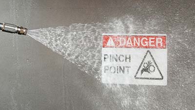 A pressure washer blasts a caution label.